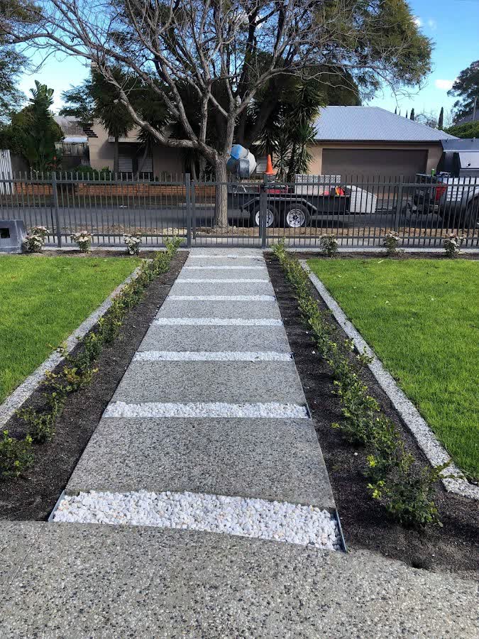 Front garden path banded with pavers and white pebble stripes between two lawns