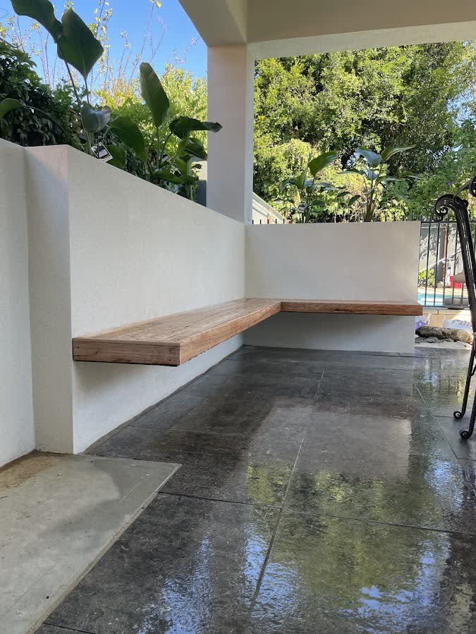 Built-in timber corner bench on a covered stone patio beside the pool