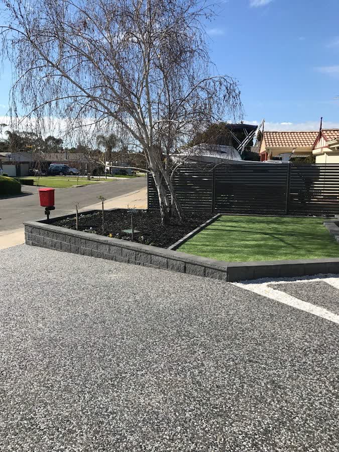 Besser-block retaining wall garden bed with fresh turf beside a gravel driveway